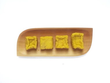 Beyaz arka planda izole edilmiş, dikdörtgen ahşap bir tabakta çiğ sarı tofu ya da sarı tofunun yakın görüntüsü..