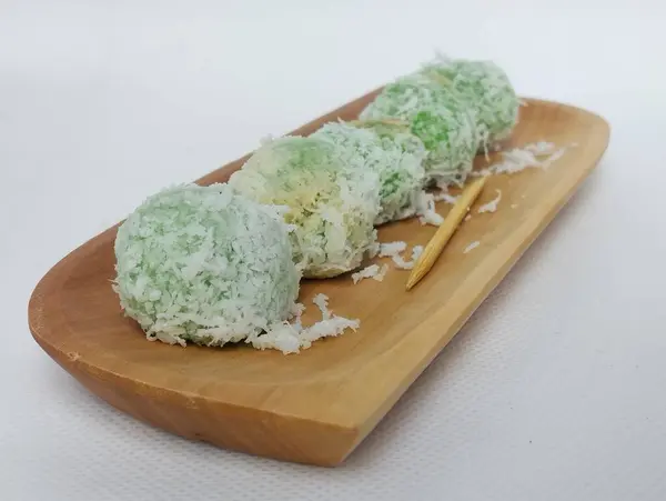 stock image klepon cake on a wooden plate, isolated with a white background. klepon cake is a typical Indonesian food that is round and green in color. 