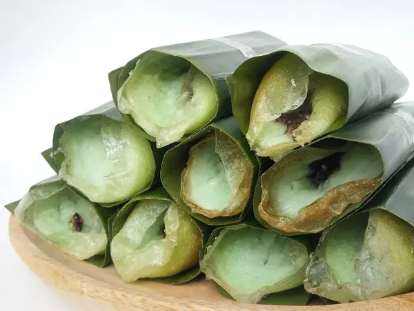 stock image Solo serabi cake wrapped in banana leaves, placed on a wooden plate and isolated against a white background - Solo serabi cake is a cake with a soft and sweet texture.