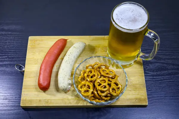 İki geleneksel Alman sosisi, kristal bir kasede çıtır kraker ve kırsal bir ahşap tepside dolu bir bira kupası..