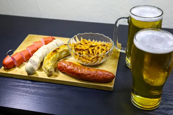 Dört Alman sosisi, iki dilimlenmiş ve iki tam çıtır kraker, bir kristal kasede tam bir bira bardağı ve ahşap bir tepsinin kenarlarına yerleştirilmiş bira bardağı içeren yakın çekim görüntüleri. Ekim Festivali için ideal.