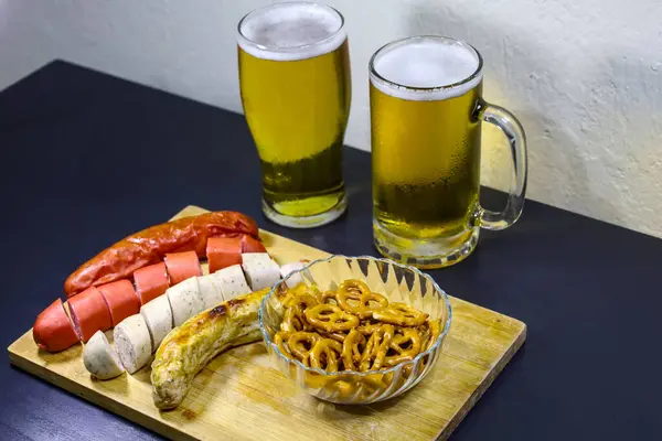 Yakın çekimde iki dilimlenmiş ve iki bütün halinde kristal bir kasede gevrek krakerlerle eşleştirilmiş çeşitli Alman sosisleri yer alıyor. Tam bir bira bardağı ve bira bardağı kırsal bir ahşap tepsinin arkasına konur, geleneği geliştirir.