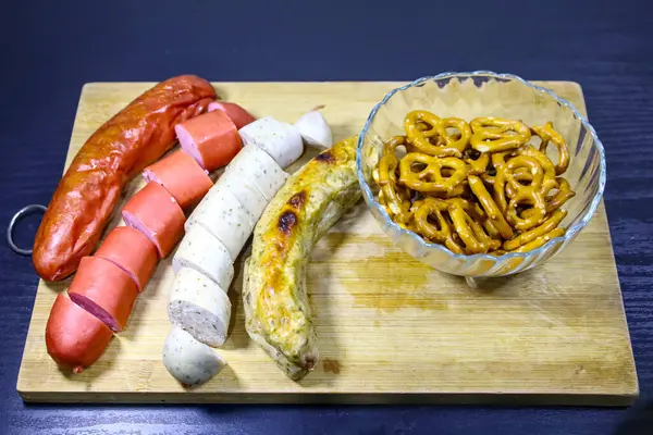 Dört sosis, iki dilimlenmiş ve bir kasede gevrek kraker bulunan yakın çekim, hepsi de ahşap bir tepside..