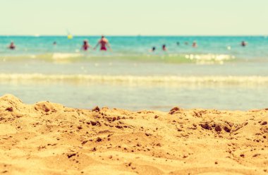 Beach sand with sea waves and bathers in the distant. Close-up of fine sand at the seashore. View as relaxing laying on towel sunbathing. Summer vacations. clipart