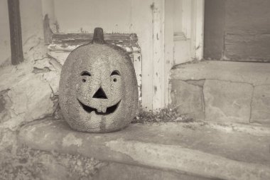 Creepy old black and white photograph of pumpkin with Jack olantern face at the steps of the front door of a house in Halloween fall season. Ancient tradition for Dia de Muertos the 1st of November.  clipart