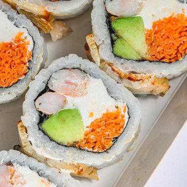 Beyaz bir tabak lezzetli bir sosla kaplı çeşitli suşi rulolarıyla doludur..