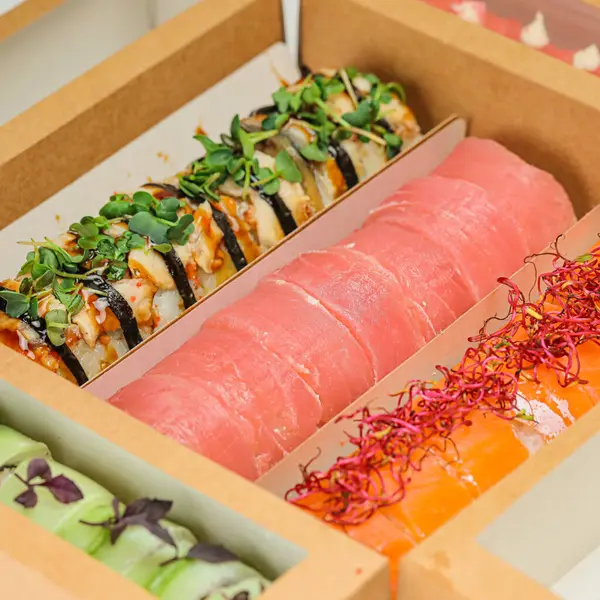 Ton balığı, somon balığı, yılan balığı ve Kaliforniya dürümleri gibi çeşitli suşi dürümleriyle dolu bir kutu, ahşap bir masada dinleniyor..