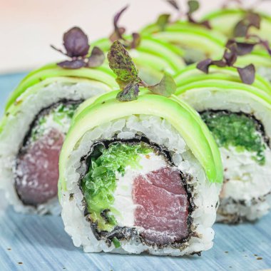 Mavi tabakta yeşil ve beyaz soslu suşi ruloları..