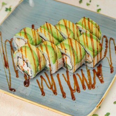 Baharatlı sosla kaplı bir suşi rulosu içeren mavi bir tabak..