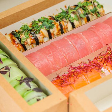 Çeşitli suşi dürümleri, nigiri ve sashimi ile dolu bir kutu. Japon mutfağının farklı lezzetleri ve dokuları sergileniyor..