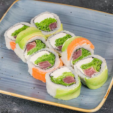 Üzerinde çeşitli suşi dürümleri olan mavi bir tabak, çeşitli aromalar, renkler ve dokular sergiliyor..