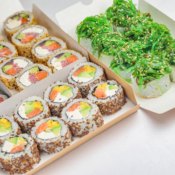 A photograph showing a box filled with sushi placed next to another box containing various types of sushi.