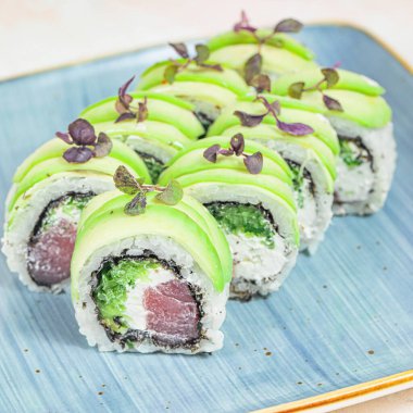 Lezzetli bir suşi tabağı sunan mavi bir tabak. Üstünde bol miktarda yeşil sos var..