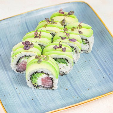 Mavi tabakta, üzerinde kremalı avokado dilimleri olan suşi ruloları var..