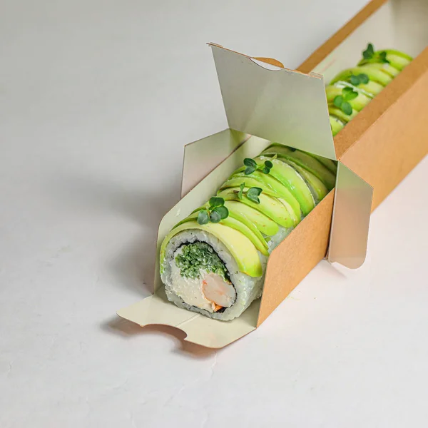 A sushi box filled with a variety of fresh green vegetables and a perfectly rolled sushi roll in the center.