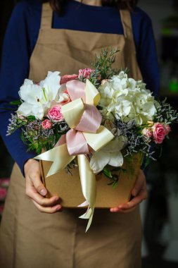Önlük takan bir kadın elinde güzel bir buket çiçek tutar ve arkasında bolca kopya bırakır..