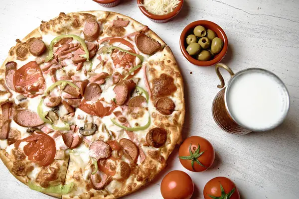 A pizza is placed on top of a table next to a cup of milk, creating an appetizing and contrasting composition.