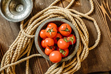 Olgun, kırmızı domateslerle dolu bir kase sağlam bir ahşap masanın üzerinde oturur..