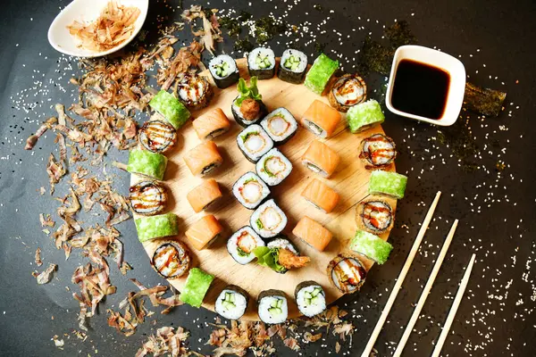 A plate filled with sushi rolls, accompanied by chopsticks and a small dish of dipping sauce.
