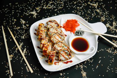 Lezzetli yiyeceklerle dolu bir tabak, yanında kullanılmaya hazır yemek çubukları ve tabağın üzerine lezzetli bir sos dökülüyor..