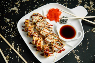 Lezzetli Asya mutfağıyla dolu bir tabağın yakın plan çekimi. Çubuklar, ısırık büyüklüğünde bir porsiyon alıp aromalı bir sosa batırıyor..