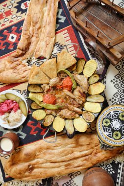 Lezzetli yiyeceklerle dolu bir tepsi desenli bir halının üzerine konur ve davetkar bir yemek takımı oluşturur..