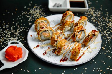 Beyaz tabak çeşitli suşi parçalarıyla süslenir, her biri bol ve lezzetli soslarla süslenir..