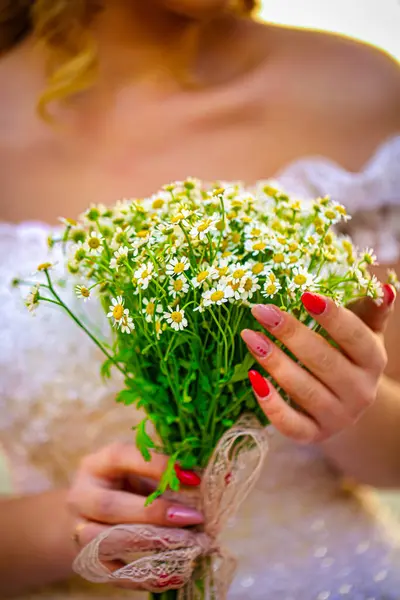 Göz kamaştırıcı bir gelin, özel gününde elinde bir buket papatya tutuyor..