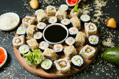 Canlı ve renkli malzemelerle çevrili çeşitli suşi dürümleriyle dolu bir tabak. Yanında da küçük bir kase soya sosu var..