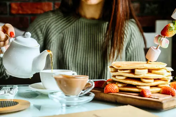 Bir kadın dikkatle çayını taze yapılmış uzun bir krep yığınına döküyor..