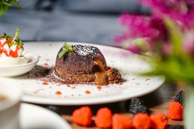 Zengin katmanlı ve böğürtlenlerle süslenmiş bir çikolatalı pasta bir tabakta oturur..