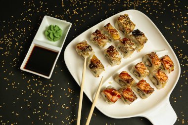 Beyaz bir tabak lezzetli suşiyle dolu ve yanında bir çift çubuk var..