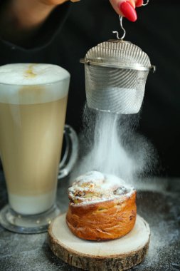 Bir insan masaya yerleştirilmiş lezzetli bir pastanın üzerine şeker döküyor..