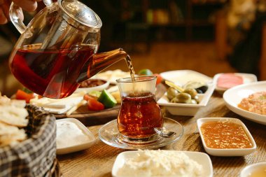 Bir insan seramik bir çaydanlıktan cam bir fincana sıcak çay dökerek dönen bir buhar bulutu yaratır..