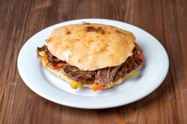 Çeşitli dolgularla dolu bir sandviç, beyaz bir tabakta, ahşap bir masanın üzerinde duruyor..