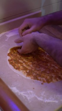 Hamur yoğuran ve mutfak tezgahında pizza yapmak için malzeme hazırlayan biri..