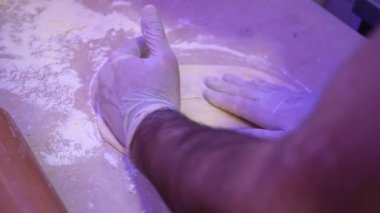 Beyaz eldiven giyen bir şahıs tezgahta hamur yoğururken görülüyor..