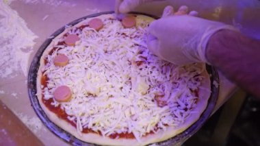 Bir insan mutfak ortamındaki pizzaya malzeme ekler..