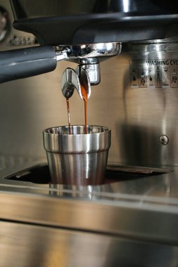 Modern bir espresso makinesi ustalıkla bekleme bardağına buharlı kahve koyar..