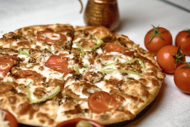 Lezzetli bir pizza, yanında taze domateslerle bir masanın üzerine yerleştirilir..