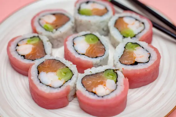 A white plate is filled with sushi rolls and accompanied by a pair of chopsticks.