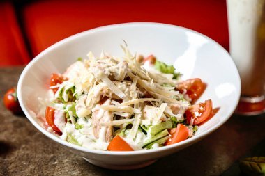 Taze salatayla dolu beyaz bir kâse ferahlatıcı bir içeceğin yanında oturup sağlıklı ve tatmin edici bir yemek oluşturur..