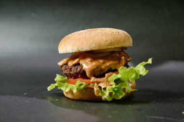 Lezzetli bir çizburger, marul ve domatesli, parlak siyah bir yüzeye yerleştirilmiş..