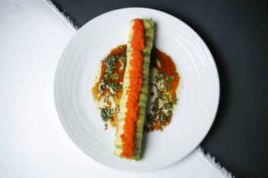 Taze salatalık dilimleriyle düzgünce düzenlenmiş beyaz bir tabak ve üzerine de lezzetli bir sos..