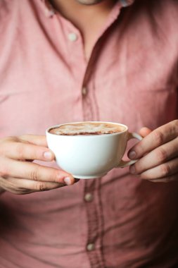 Elinde bir fincan kahve tutan bir adam, bir yudum alıyor ve sıcaklığın tadını çıkarıyor..