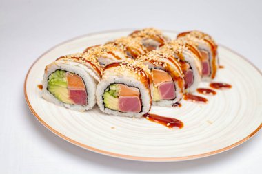 Suşi dolu beyaz bir tabak sergilenen bir fotoğraf. Üzeri bol baharatlı sosla kaplı..