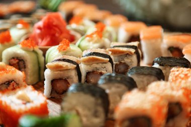 Yakından çekilmiş bir fotoğraf, yanında küçük bir tabak soya sosu eşliğinde farklı suşi rulolarından oluşan yeni sarılmış bir tabak sunuyor..