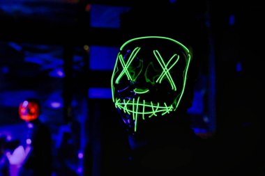 Aydınlatılmış neon maske takan biri karanlık bir odada duruyor..