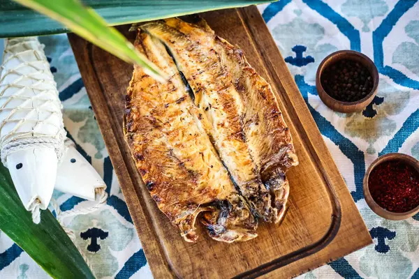 stock image A wooden cutting board with a fish placed on top, resting on a table.