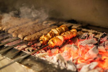 Sosisli ve sosisli ızgarada pişiyor. Alevler ve dumanlar yükseliyor..